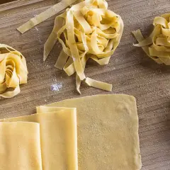 Frischer, selbstgemachter Pastateig, wie im original italienischen Rezept, liegt auf einem Holzbrett. Tagliatelle-Nester und Teigplatten warten auf ihre Zubereitung.