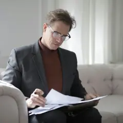 Hombre con gafas revisa documentos en un sofá, concentrado en su trabajo. ¿Qué es la fein? Es la dedicación a los detalles.