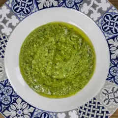 Un plato blanco con un vibrante pesto genovese, adornado con un borde de azulejos azules y grises.