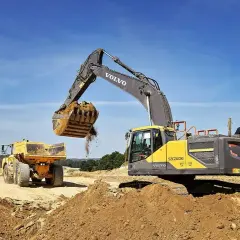 Koparka Volvo wysypuje ziemię do wywrotki. Prace ziemne, ułożenie rur w wykopie cennik bez materiału.