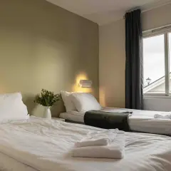 Två bäddade sängar med vita lakan och handdukar på Ekerums Resort. En vas med blommor står på nattduksbordet.