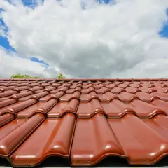 Czerwona dachówka ceramiczna lśni w słońcu. Zastanawiasz się, jaka dachówka ceramiczna najlepsza? Ta prezentuje się okazale.