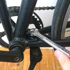 Montaż stopki rowerowej. Klucz dokręca śrubę mocującą stopkę do ramy roweru, obok korby i łańcucha.