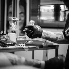Artysta tworzy skomplikowany ornament tattoo na ręce klienta. Widać maszynkę, tusze i przygotowania do sesji.