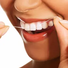 Uśmiechnięta osoba używa nić dentystyczną do czyszczenia zębów. Dbałość o higienę jamy ustnej jest ważna.