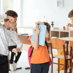 Chłopiec zasłania się zeszytem, podczas gdy inni uczniowie w klasie wydają się być zaangażowani w bullying.