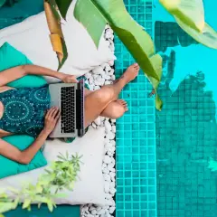 Kobieta pracująca na laptopie przy basenie. Tak żyją dzisiejsi nomadzi, kto to taki? Wolność i praca w dowolnym miejscu.