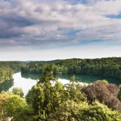 Malownicze lubuskie atrakcje: jezioro otoczone gęstym lasem, z fragmentem czerwonego dachu na brzegu.