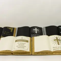Otwarta książka na cmentarz, złota, z napisem "Pamiętamy" i krzyżem. Obok inne nagrobki w kształcie ksiąg.