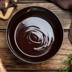 Lśniąca polewa kakaowa w misce, obok kawałki czekolady, trzepaczka i listki mięty.