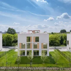 Nowoczesne budynki Ronson Nova Królikarnia z dużymi oknami i zielonymi trawnikami pod błękitnym niebem.