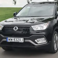 Czarny SsangYong Tivoli, model suw 2000, pędzi po wiejskiej drodze wśród zielonych pól.