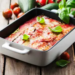 Lasagne courgette gratinée, garnie de basilic frais, sur fond de bois rustique avec des tomates cerises et des courgettes.