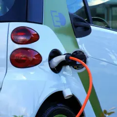 Voiture électrique blanche en charge, avec un câble orange branché. Le symbole "E" vert sur le flanc indique son caractère écologique. Le frais réel d'une voiture électrique est sa recharge.