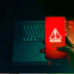 Dłoń trzyma smartfon z czerwonym ekranem i ostrzeżeniem o złośliwym oprogramowaniu. To może być początek oszustwa na blik.