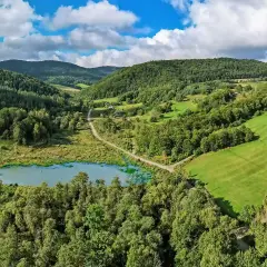 Malowniczy krajobraz Beskidu Niskiego z jeziorem, lasami i zielonymi wzgórzami. W oddali widać domki.
