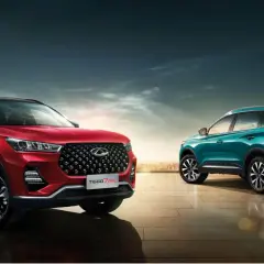 Dwa stylowe chińskie samochody, czerwony i turkusowy SUV, prezentują się na tle miejskiego krajobrazu i nowoczesnej architektury.