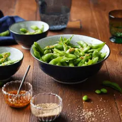 Schon gewusst, was ist Edamame? Grüne Sojabohnen in Schoten, gewürzt mit Sesam und Chili, serviert in Schalen auf Holztisch.