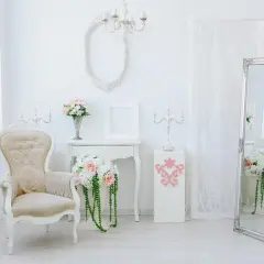 Eleganckie wnętrze w stylu shabby chic: kremowa sofa, wazon z kwiatami, lustro i świeczniki tworzą romantyczną atmosferę.