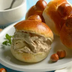 Brioche col tuppo ripieno di gelato, con nocciole e biscotti intorno.