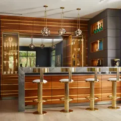 Luxurious home bar ideas featuring a marble countertop, wood cabinetry, gold bar stools, and a wine display.