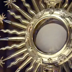 Złota monstrancja z hostią, symbolizująca adorację. Promienie ozdobione aniołkami i kwiatami.