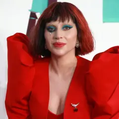 Lady Gaga w czerwonym, teatralnym stroju z niebieskim makijażem oczu i łzą na policzku. Fani marzą o koncercie Lady Gaga w Polsce.