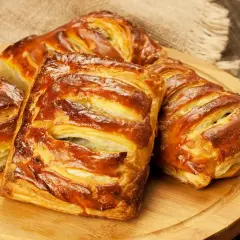 Złociste, pieczone ciasto francuskie z nadzieniem, ułożone na drewnianej desce.