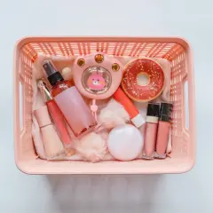 Rosa korg med smink på flyget: läppglans, puder, parfymflaska och en söt liten fläkt.