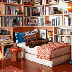 Gemütliches Lesezimmer einrichten mit Bücherregalen voller Bücher, einem Bett, einem Ledersessel und einem roten Stuhl.