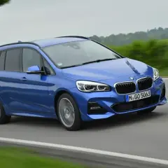 Niebieskie BMW 220i na drodze, z zielonymi polami po bokach.