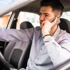 Mężczyzna za kierownicą rozmawia przez telefon, martwiąc się o mandaty w Szwajcarii.