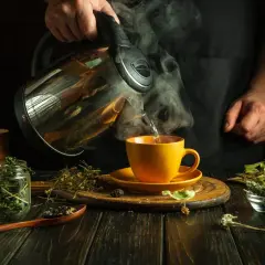 Heißer Kräutertee wird in eine gelbe Tasse gegossen. Ein Hausmittel gegen körperliche Erschöpfung, zubereitet aus getrockneten Kräutern.