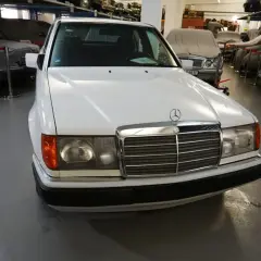Biały Mercedes "Baleron" z lat 80. stoi w muzeum obok innych zakrytych samochodów.