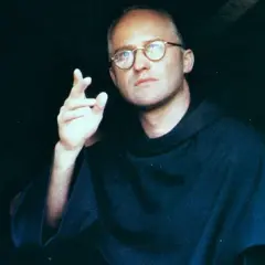 Aktor w filmie o Maksymilianie Kolbe, w okularach i habicie, gestykuluje.