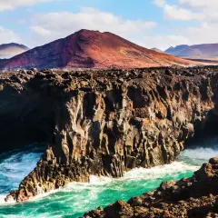 Wulkaniczne klify na Lanzarote, turkusowe morze i góry w oddali. Idealna pogoda na odkrywanie tej wyspy.