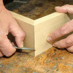Präzises Gehrung schneiden: Hände führen ein scharfes Werkzeug an Holzleisten entlang, um eine perfekte Ecke zu schaffen. Ein kleiner Trick für saubere Verbindungen.