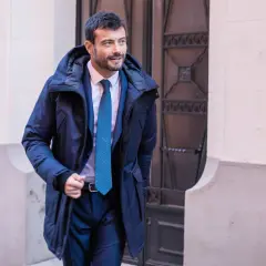 Un homme élégant porte un type de manteau homme bleu marine, un costume et une cravate, marchant dans la rue.
