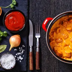 Pyszne parówki w sosie śmietanowym – idealny pomysł, co zrobić z parówek na obiad. Obok składniki: cebula, ketchup, przyprawy.