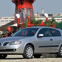Srebrny Nissan Almera stoi przed czerwoną, industrialną konstrukcją.