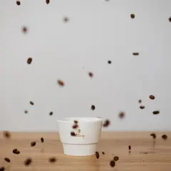 Kaffeebohnen tanzen um eine weiße Tasse. Der Duft verspricht vollen Kaffee Geschmack.