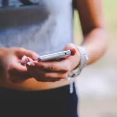 Dłonie z zadbanymi paznokciami trzymają srebrny telefon. To zrzut ekranu Samsunga, uchwycony w letnim otoczeniu.