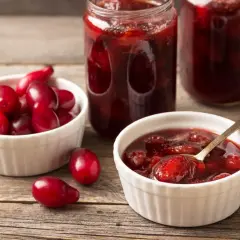 Słoiki i miseczki pełne aromatycznej konfitury z derenia, obok świeże owoce.