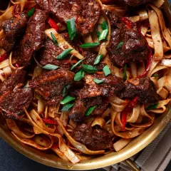Wołowina po syczuańsku z makaronem, papryczkami chili i szczypiorkiem w złotej misie.