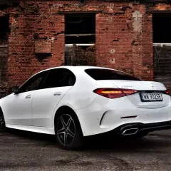 Biały Mercedes C 220 d z czarnymi felgami na tle zrujnowanej ceglanej ściany.