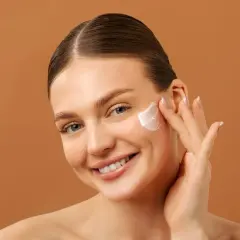 Mujer sonriente aplicándose crema facial. Una rutina de belleza con retinol y vitamina c para una piel radiante.