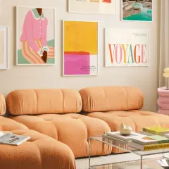 Ein orangefarbenes Sofa mit bunten Bildern an der Wand. Welche Farbe passt zu Orange? Pink und Gelb harmonieren hier perfekt.