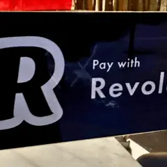 Znak informuje, jak płacić Revolutem. Widoczny duży symbol "R" i napis "Pay with Revolut".