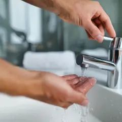 Dłoń pod strumieniem wody z kranu w łazience.