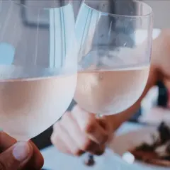 Dwie osoby wznoszą toast schłodzonym, różowym winem. Idealne na letnie popołudnie.